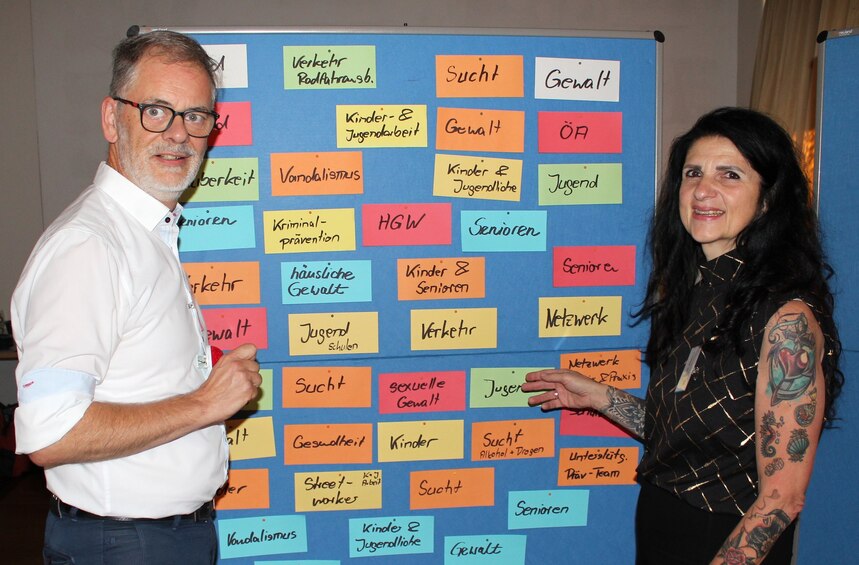 Zwei Personen stehen neben einem Flipchart und schauen in die Kamera.