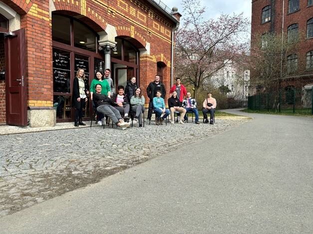 Auf dem Bild sieht man 13 Personen in zwei Reihen vor einem Backsteingebäude. 7 Personen sitzen und 6 stehen dahinter.